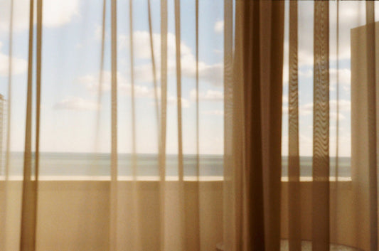 Soft sheer curtains with sunlight streaming through, revealing the calm ocean and sky beyond.